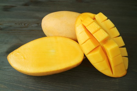 Fresh Ripe Thai Nam Dok Mai Mangoes Whole Fruit and Cut in Half on Dark Brown Wooden Backgroundの写真素材