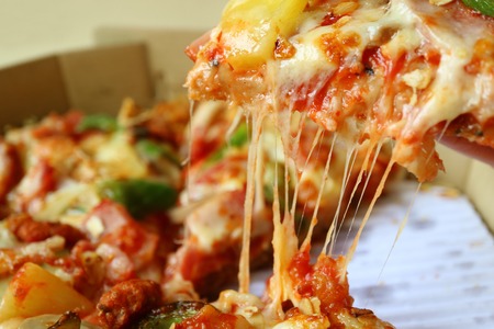 Closed Up a Slice of Pizza with Stretching Cheese Being Taken from Paper Boxの写真素材