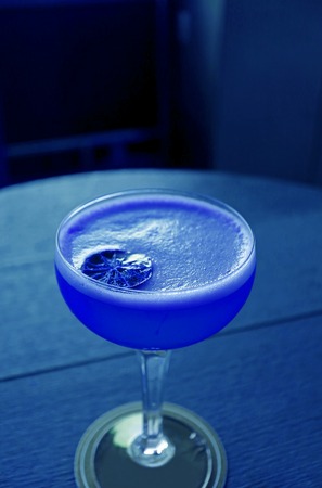 Vertical image of a glass of cocktail isolated on the round table in vivid blue color