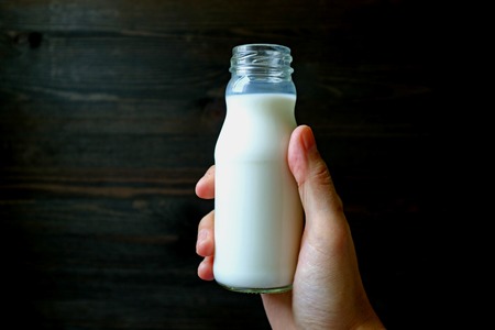Man's hand holding opened bottle of milk with dark colored wall in background