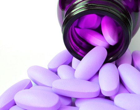 Closeup pastel purple supplement tablets spilling from glass bottle on white backgroundの写真素材