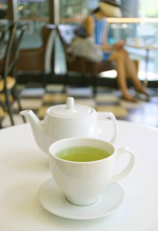Vertical image of a cup of green tea and teapot on white table in a cafeの写真素材