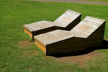 Pair of wooden benches on the lawn in the sunlight in public parkの写真素材