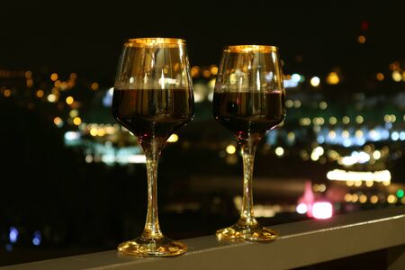 Two Wine Glasses on the Balcony with Blurry City Night View in the Backgroundの写真素材
