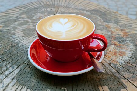 Hot Cappuccino Coffee in Red Cup Served on Tree Stump Tableの写真素材