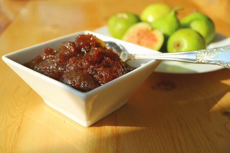 Homemade fig jam with a plate of green fresh figs in backgroundの写真素材