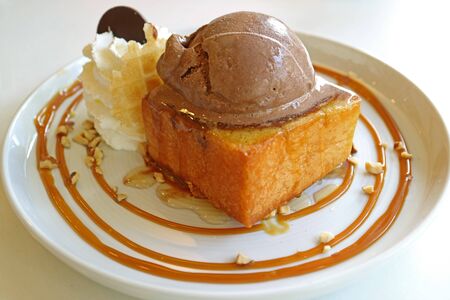 Closeup honey butter toast topped with chocolate ice cream and maple syrup on white plate