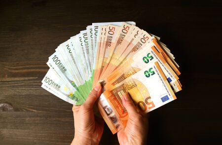 Bundle of Euro Banknotes in Female's Hand Against Dark Brown Wooden Background