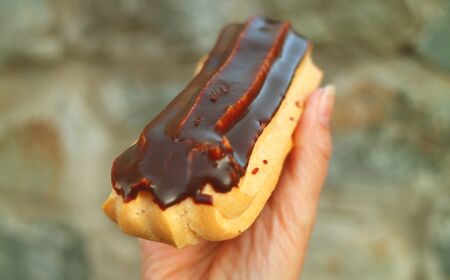 Closeup a Mouthwatering Chocolate Eclair in Hand