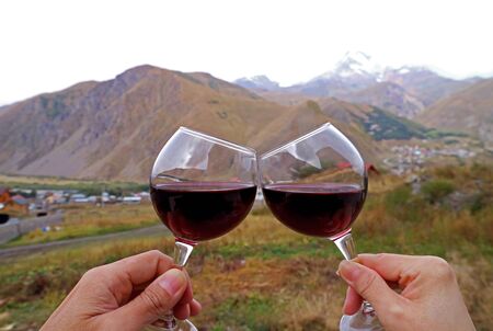 Hands holding wine glasses clinking with blurry mountains view in the backdrop