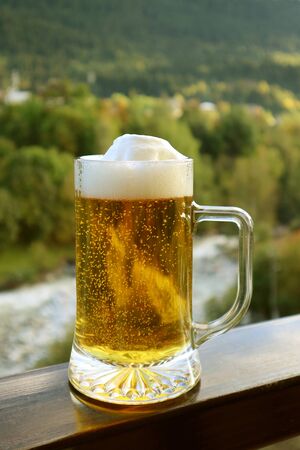 Vertical image of a pint of draft beer on the balcony railing with blurry forest viewの写真素材