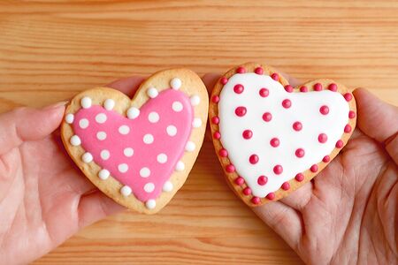 Pink and white dotted heart shaped cookies in couple's hands put together on wooden backgroundの写真素材