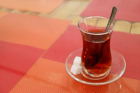Hot Turkish Tea in Tulip-shaped Glass with Sugar Cubes Isolated on Colorful Luncheon Matsの写真素材
