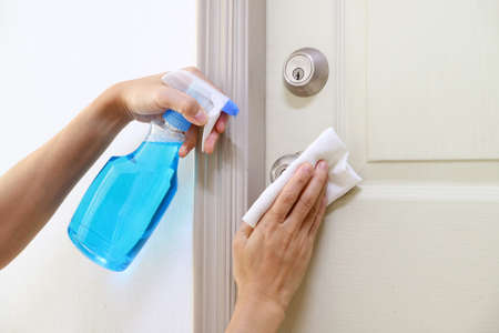 Man's hands holding alcohol cleaner bottle for cleaning room's door handleの写真素材