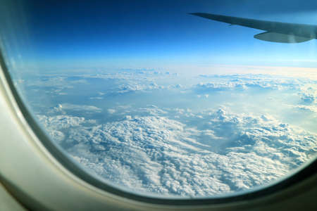 Blue sky and white clouds with airplane wing as seen from the plane window during flight