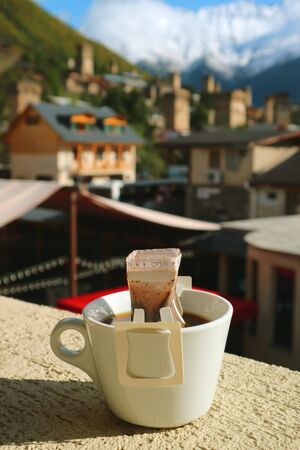 Cup of Portable Drip Coffee Being, Prepared at Outdoor Seat with Blurry Mestia Town in Background, Caucasus, Georgiaの写真素材