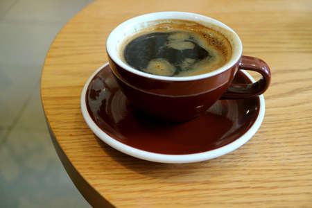 Hot coffee in dark brown cup isolated on round wooden tableの写真素材