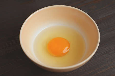 Closeup of a Fresh Raw Egg Yolk and White in a Bowl Isolated on Wooden Table