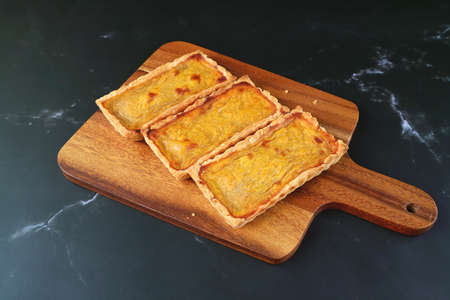 Three Delectable Pumpkin Tartlets on the Wooden Breadboard Isolated on Black Kitchen Table