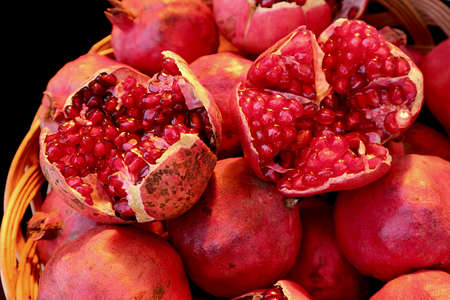 Closeup Vibrant Red Opened Fresh Pomegranate Fruits on the Whole Fruit Pileの写真素材