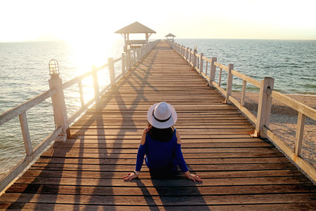 Young Woman in White Hat Sitting on the Wooden Pierの写真素材
