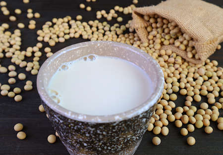 Cup of Soy Milk Isolated on the Table with Blurry Soybeans Scattered from Burlap Bagの写真素材