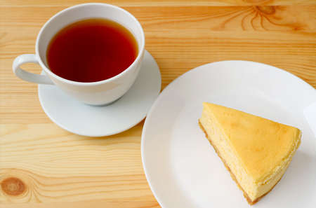 Cup of Hot Tea with a Plate of Baked Cheesecake Served on Wooden Tableの写真素材