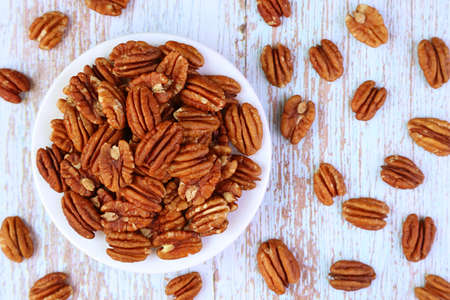 Plate Full of Pecan Nuts with Some Kernels Scattered on Wooden Table