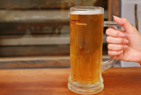 Woman's hand holding a pint of chilled beer putting on wooden tableの写真素材