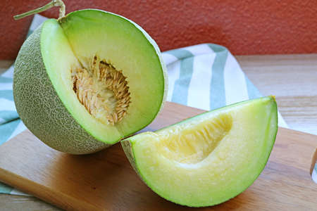Fresh Ripe Muskmelon with a Juicy Slice Cut from Whole Fruit on Wooden Cutting Boardの写真素材