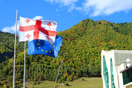 Georgian flag with EU Flag Waving Against the Early Autumn Hills of Mestia Town, Svaneti Region,...