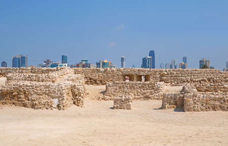 Ruins of the Bahrain Fort or Qal'at al-Bahrain with Manama Modern Cityscape in the Backdrop, Bahrainのeditorial素材