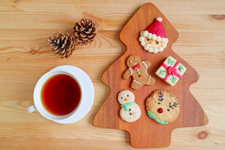 Top View of Assorted Christmas Cookies with a Cup of Hot Tea and Dry Pine Cones Served on Wooden...