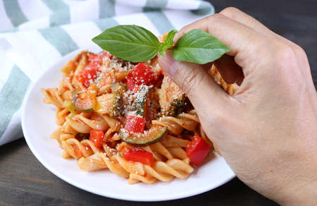 Hand Placing Basil leaves on a Dish of Fresh Cooked Whole Wheat Fusilli Pasta in Tomato Sauceの写真素材