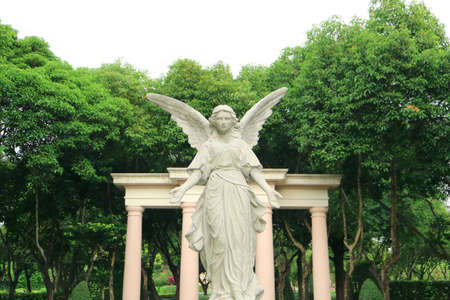 Beautiful sculpture of an angel in the lush gardenの写真素材