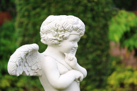 Closeup of an adorable smiling cupid sculpture in the gardenの写真素材