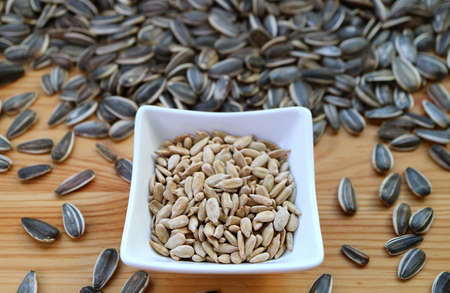 Bowl of roasted sunflower seeds with heap of raw seeds scattered around