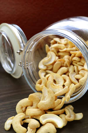 Heap of Casshew Nuts Scattered from a Glass Jar on Wooden Tableの写真素材