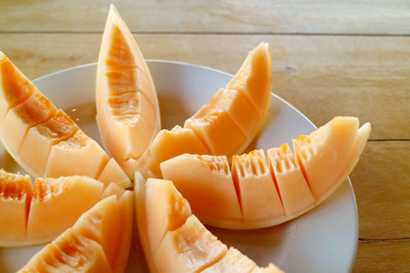Closeup Slices of Mouthwatering Fresh Juicy Cantaloupe Melon on White Plateの写真素材