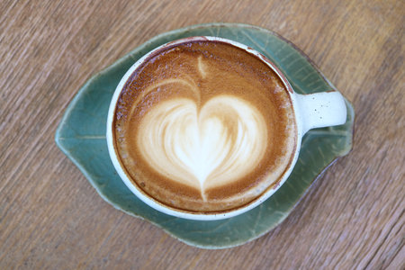 Hot cappuccino coffee with heart shaped latte art on wooden tableの写真素材