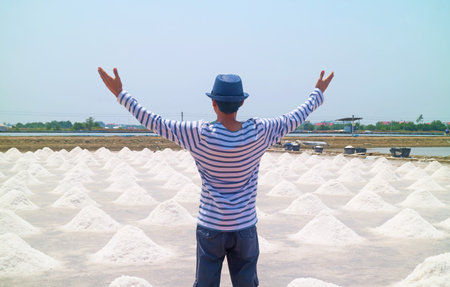 Man with arms outstretched to the sprawling salt pan in the harvest season, Samut Sakhon province of Thailandの写真素材