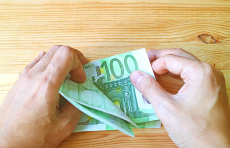 Man's Hand Holding a Bundle of 100 EURO Banknotes on Wooden Backdropの写真素材