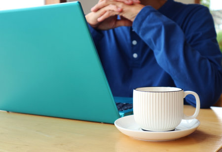 Closeup of a cup of coffee with a man working on laptop in the backdropの写真素材