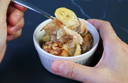Hand Scooping Mouthwatering Banana Walnut Bread Pudding from a Ceramic Bowlの写真素材