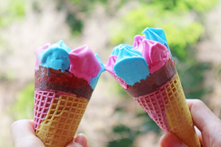 Two of Pink and Blue Ice Cream Cones Clinking on Green Foliage Background