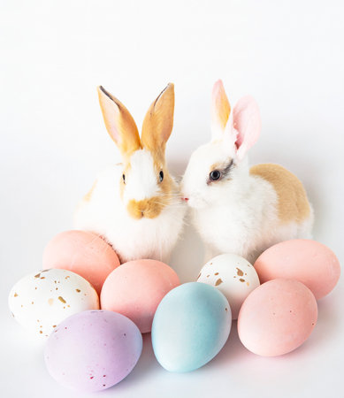 Heap of pastel colored easter eggs with a pair of adorable bunnies on white backgroundの素材