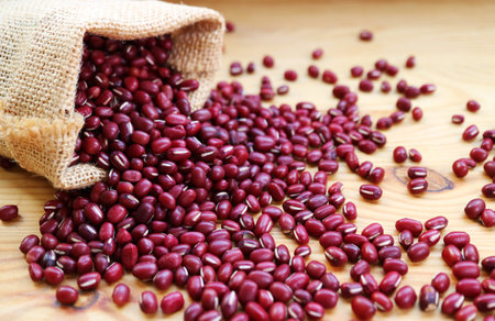 Dried Adzuki Red Beans Scattered from Burlap Bag on to Wooden Tableの写真素材
