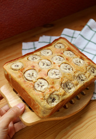 Hand Placing Freshly Baked Homemade Banana Cake on Kitchen Tableの写真素材