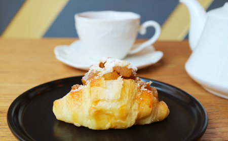Delectable Caramel Apple Cream Cheese Croissant with Blurry Teacup in the Backdropの写真素材