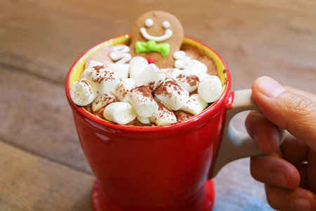 Hand Holding a Cup of Hot Chocolate with Pile of Marshmallow Candies and Gingerbread Man Cookies